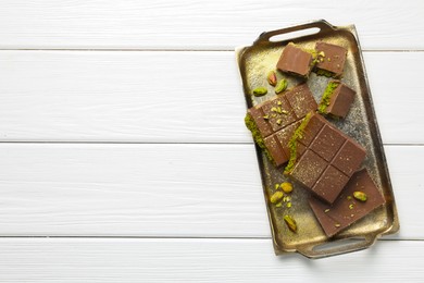 Photo of Pieces of Dubai chocolate bars with pistachios and knafeh on white wooden table, top view. Space for text