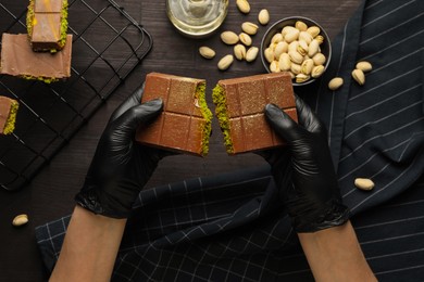 Photo of Woman breaking Dubai chocolate bar with pistachios and knafeh at wooden table, top view