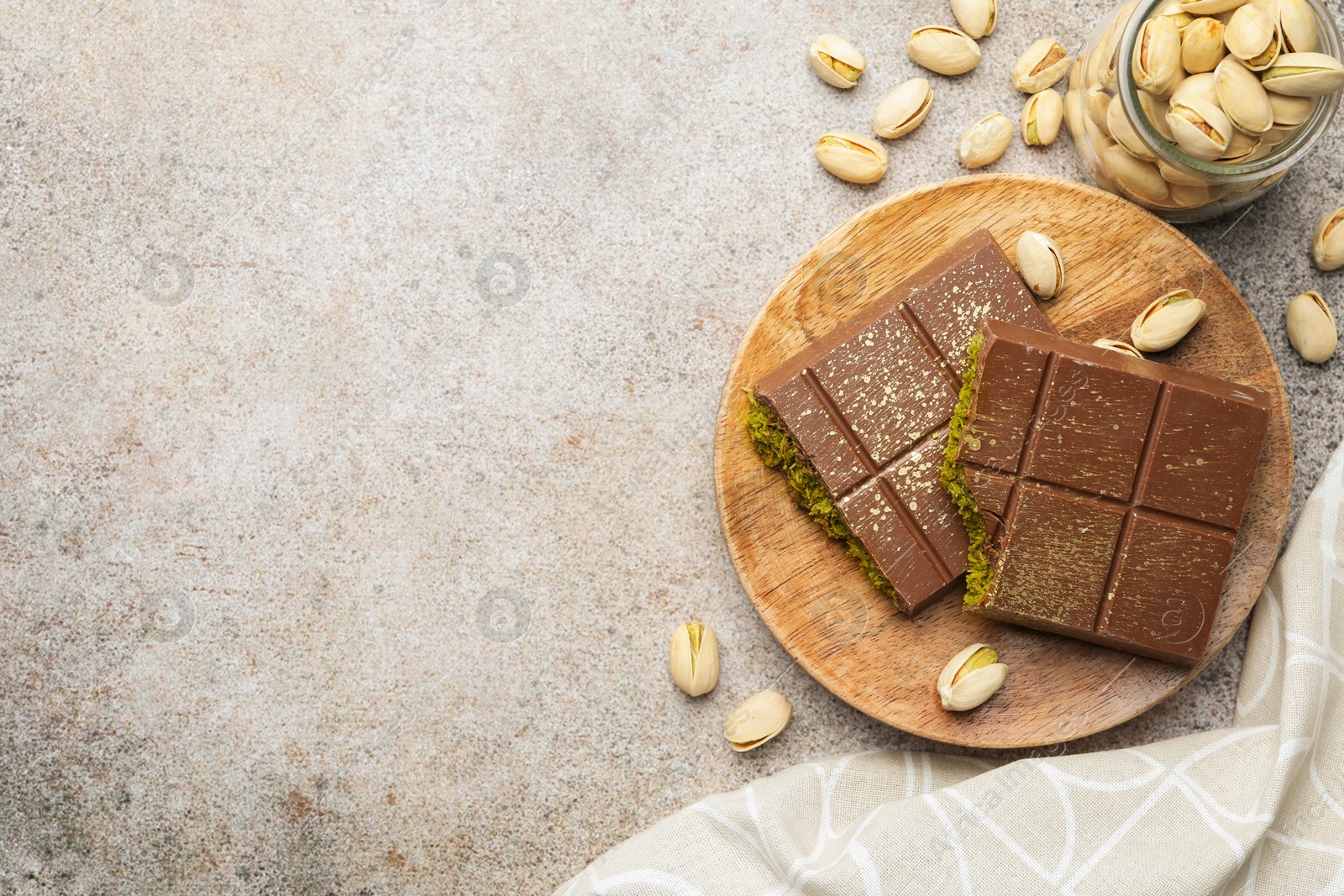 Photo of Pieces of Dubai chocolate bar with pistachios and knafeh on grey table, flat lay. Space for text