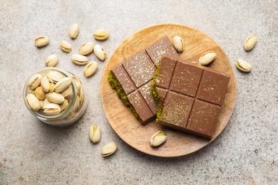 Photo of Pieces of Dubai chocolate bar with pistachios and knafeh on grey table, flat lay