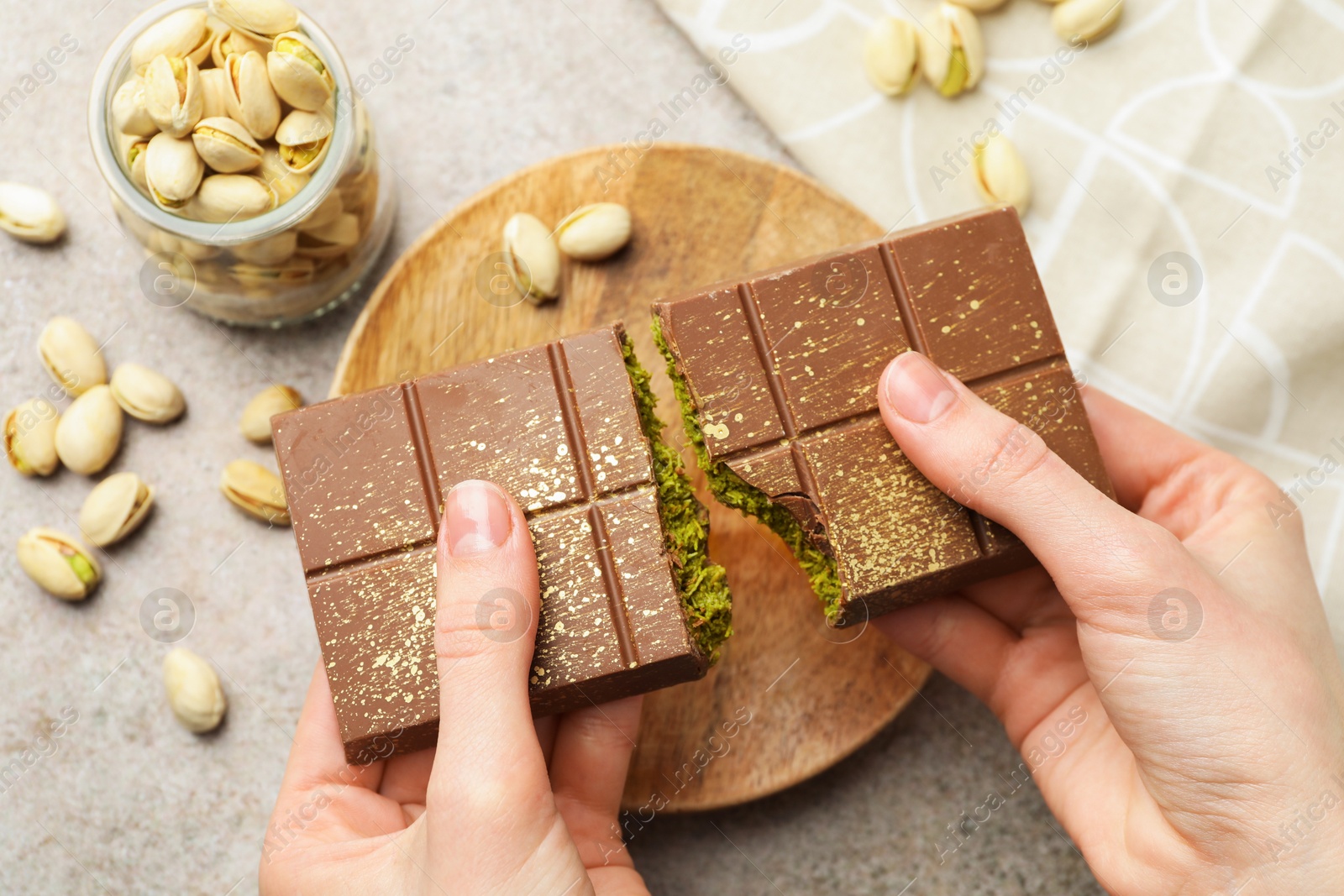 Photo of Woman breaking Dubai chocolate bar with pistachios and knafeh at grey table, closeup