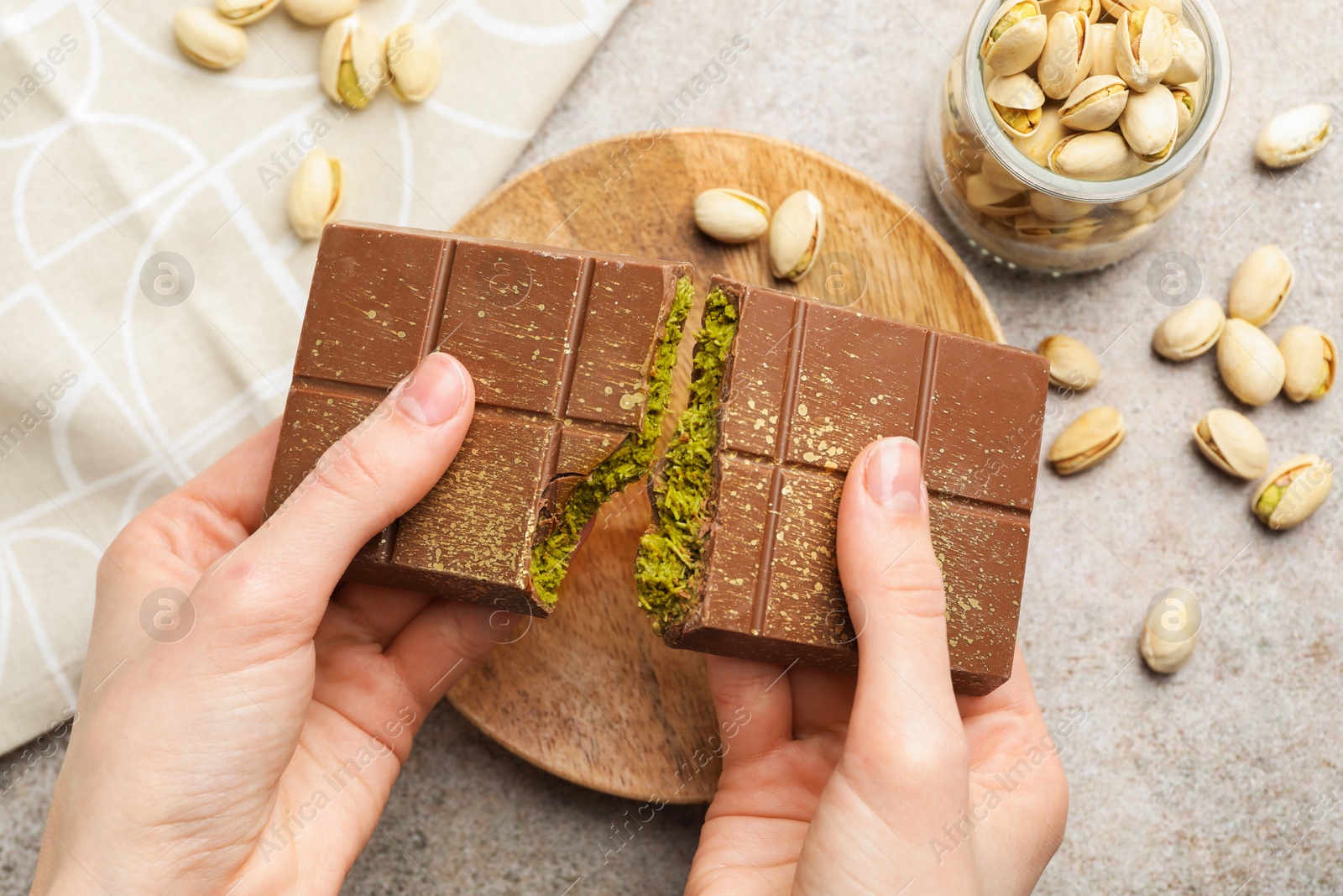 Photo of Woman breaking Dubai chocolate bar with pistachios and knafeh at grey table, closeup