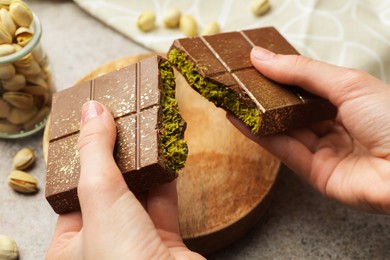 Photo of Woman breaking Dubai chocolate bar with pistachio and knafeh at grey table, closeup