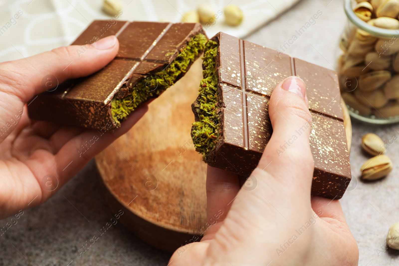 Photo of Woman breaking Dubai chocolate bar with pistachio and knafeh at grey table, closeup