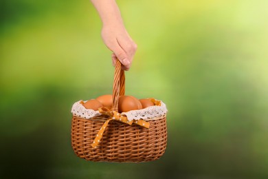 Photo of Woman with basket of raw eggs on blurred background, closeup