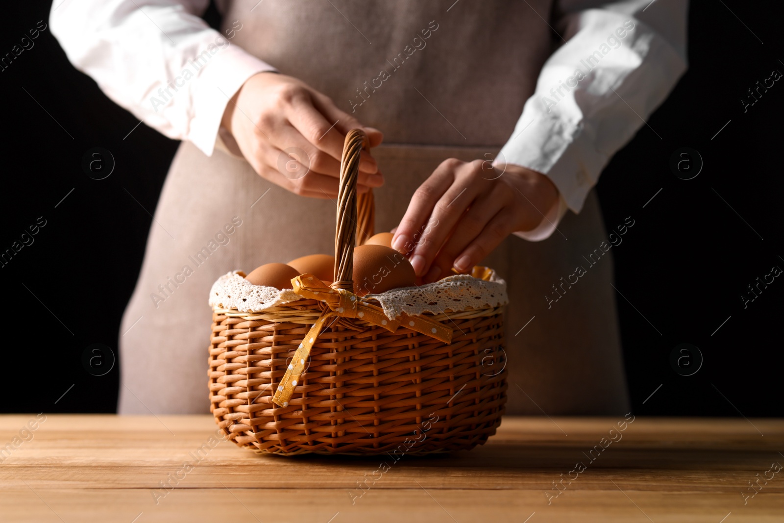 Photo of Woman with basket of raw eggs at wooden table, closeup