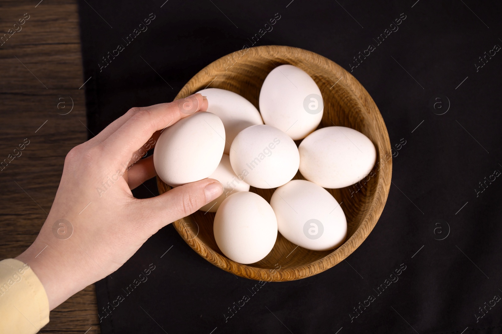 Photo of Woman with raw eggs at wooden table, top view