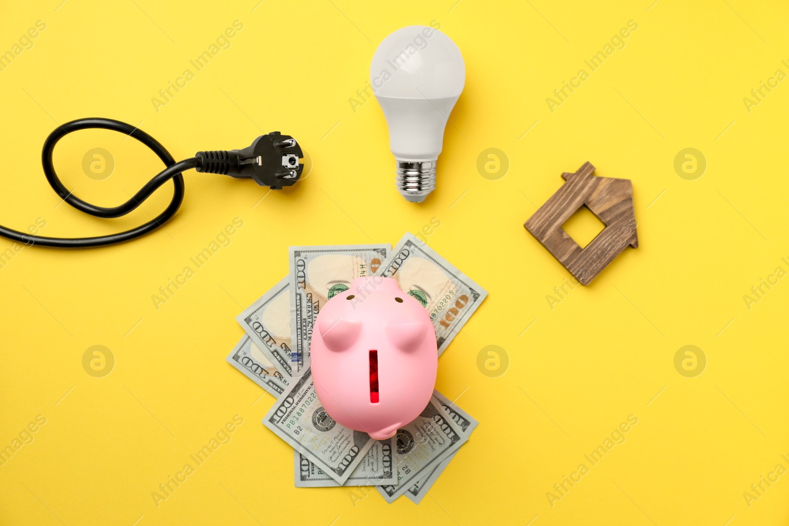 Photo of Piggy bank, dollar banknotes, light bulb, plug and house model on yellow background, flat lay. Energy saving concept