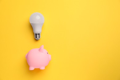 Photo of Light bulb and piggy bank on yellow background, flat lay. Energy saving concept