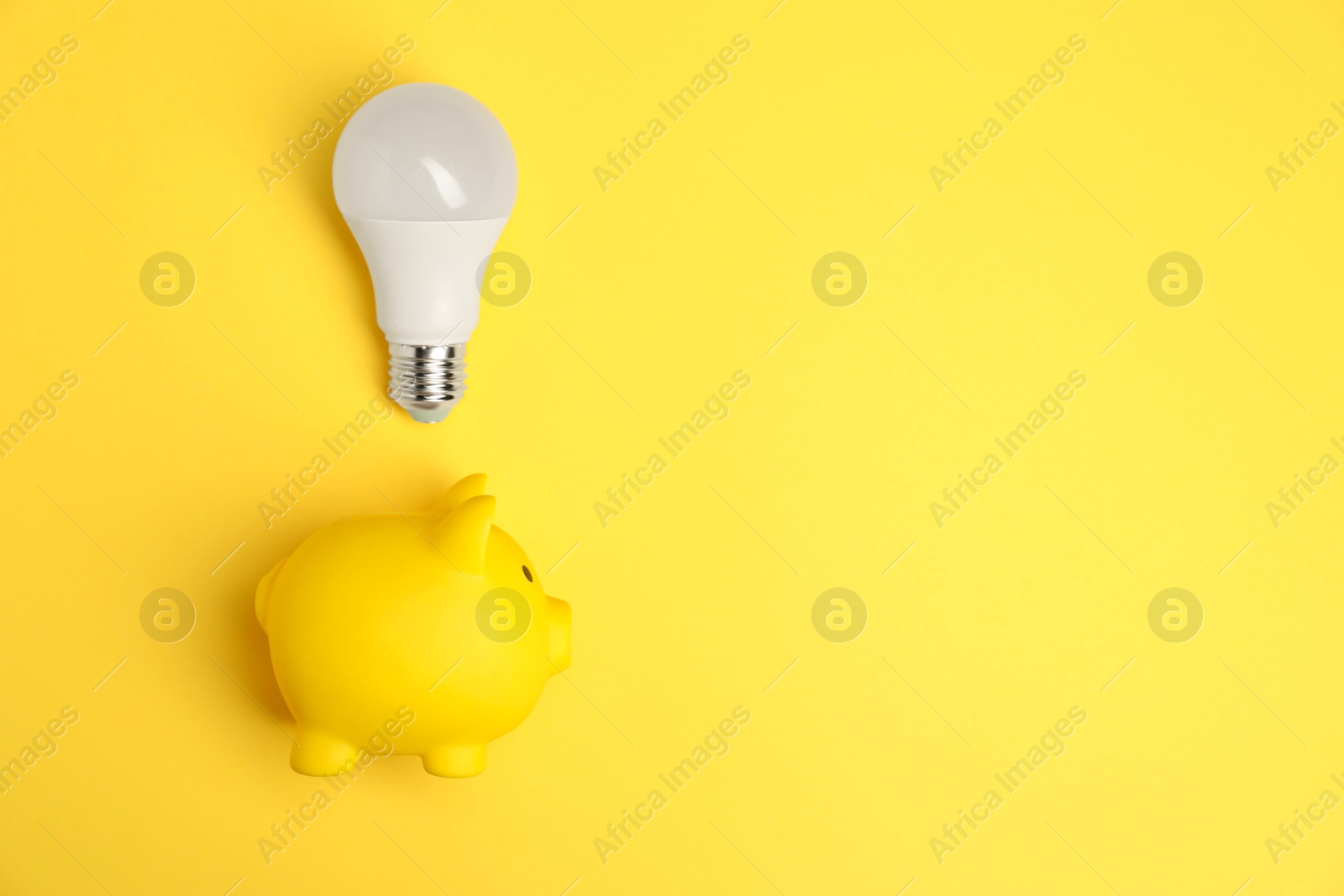 Photo of Light bulb and piggy bank on yellow background, flat lay with space for text. Energy saving concept