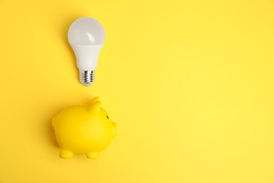 Photo of Light bulb and piggy bank on yellow background, flat lay with space for text. Energy saving concept