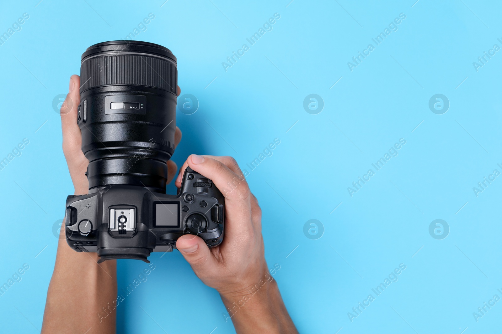 Photo of Photographer with professional camera on light blue background, top view. Space for text