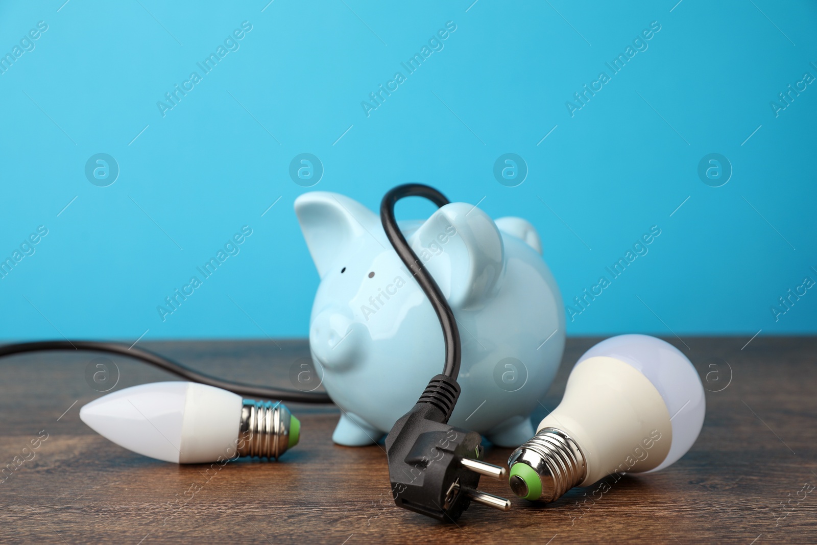 Photo of Piggy bank, plug and light bulbs on wooden table, closeup. Energy saving concept