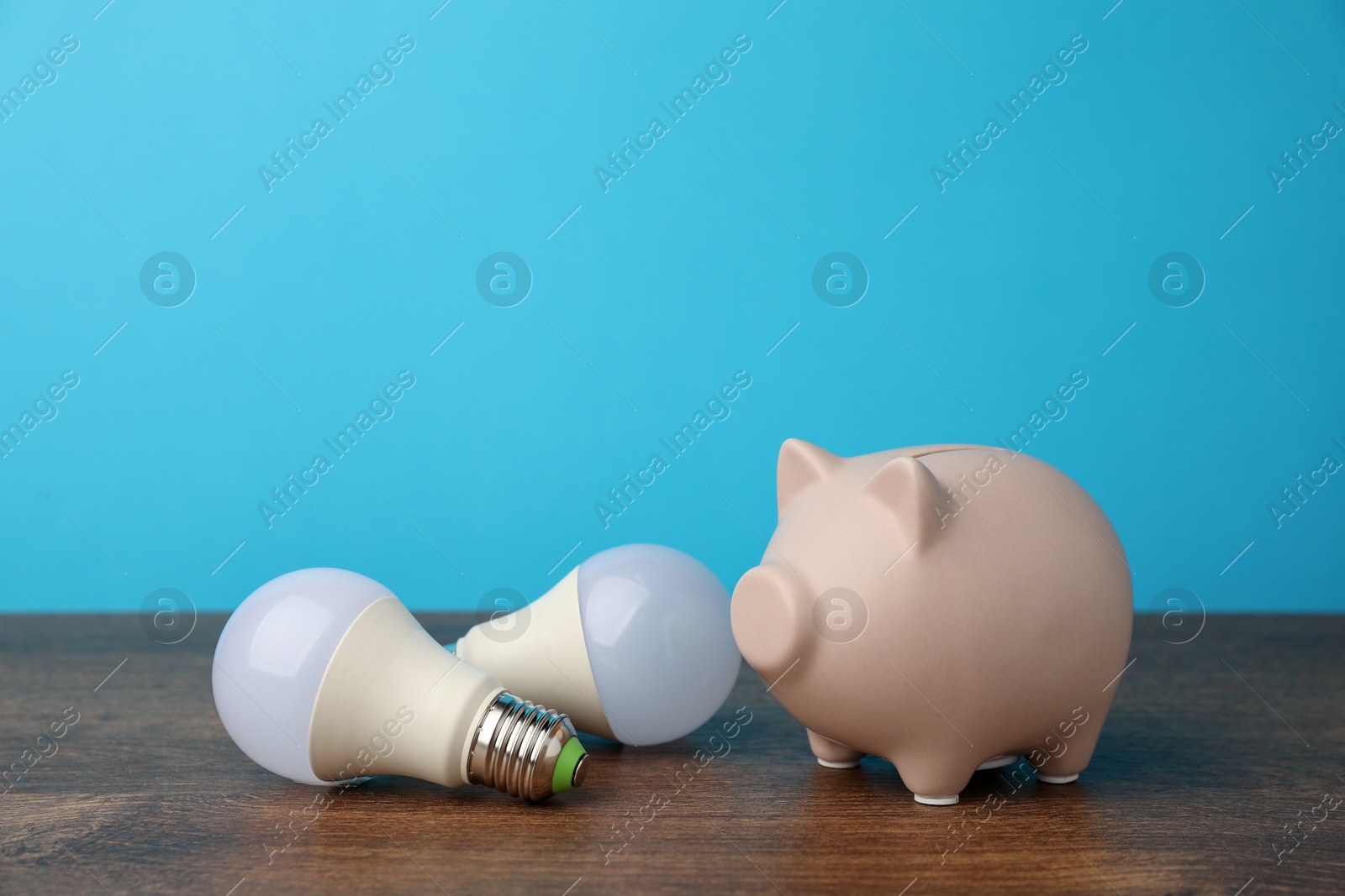 Photo of Piggy bank and light bulbs on wooden table. Energy saving concept