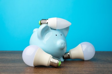 Photo of Piggy bank and light bulbs on wooden table. Energy saving concept