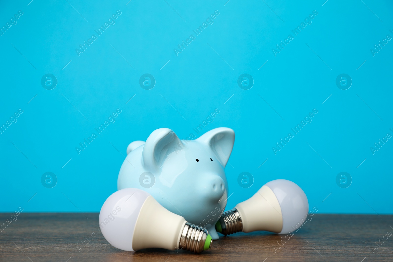 Photo of Piggy bank and light bulbs on wooden table. Energy saving concept