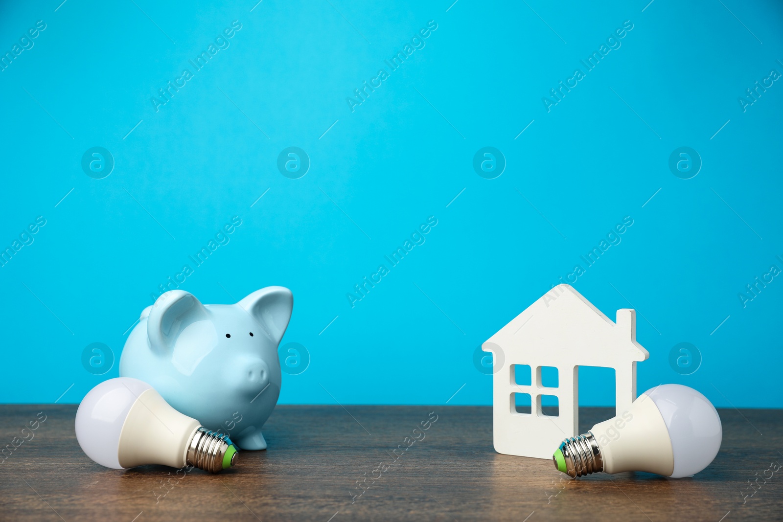 Photo of Piggy bank, house model and light bulbs on wooden table. Energy saving concept