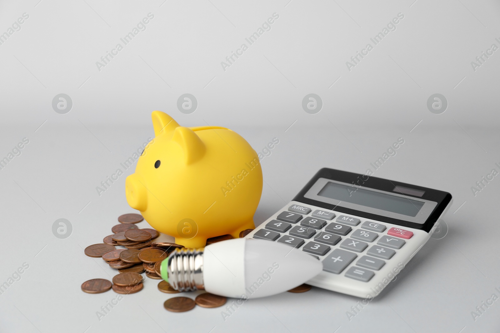 Photo of Piggy bank, coins, calculator and light bulb on grey background, closeup. Energy saving concept