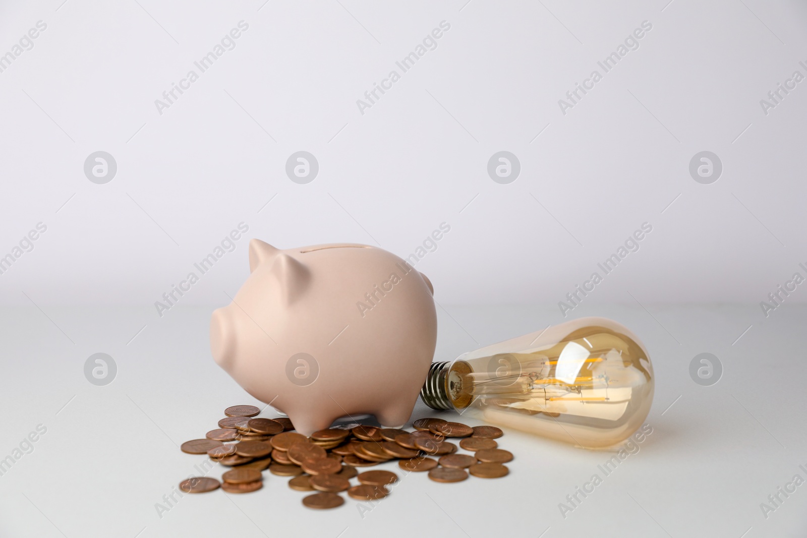 Photo of Piggy bank, coins and light bulb on grey background, closeup. Energy saving concept