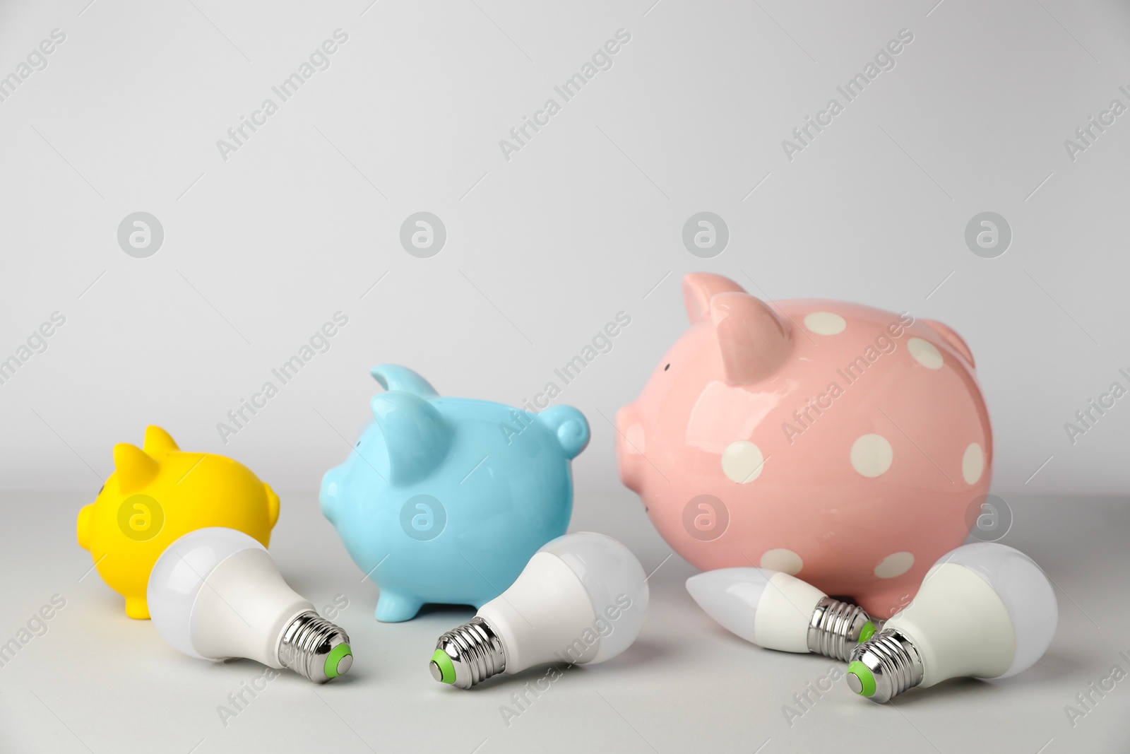 Photo of Piggy banks and light bulbs on grey background. Energy saving concept