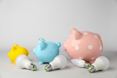 Photo of Piggy banks and light bulbs on grey background. Energy saving concept