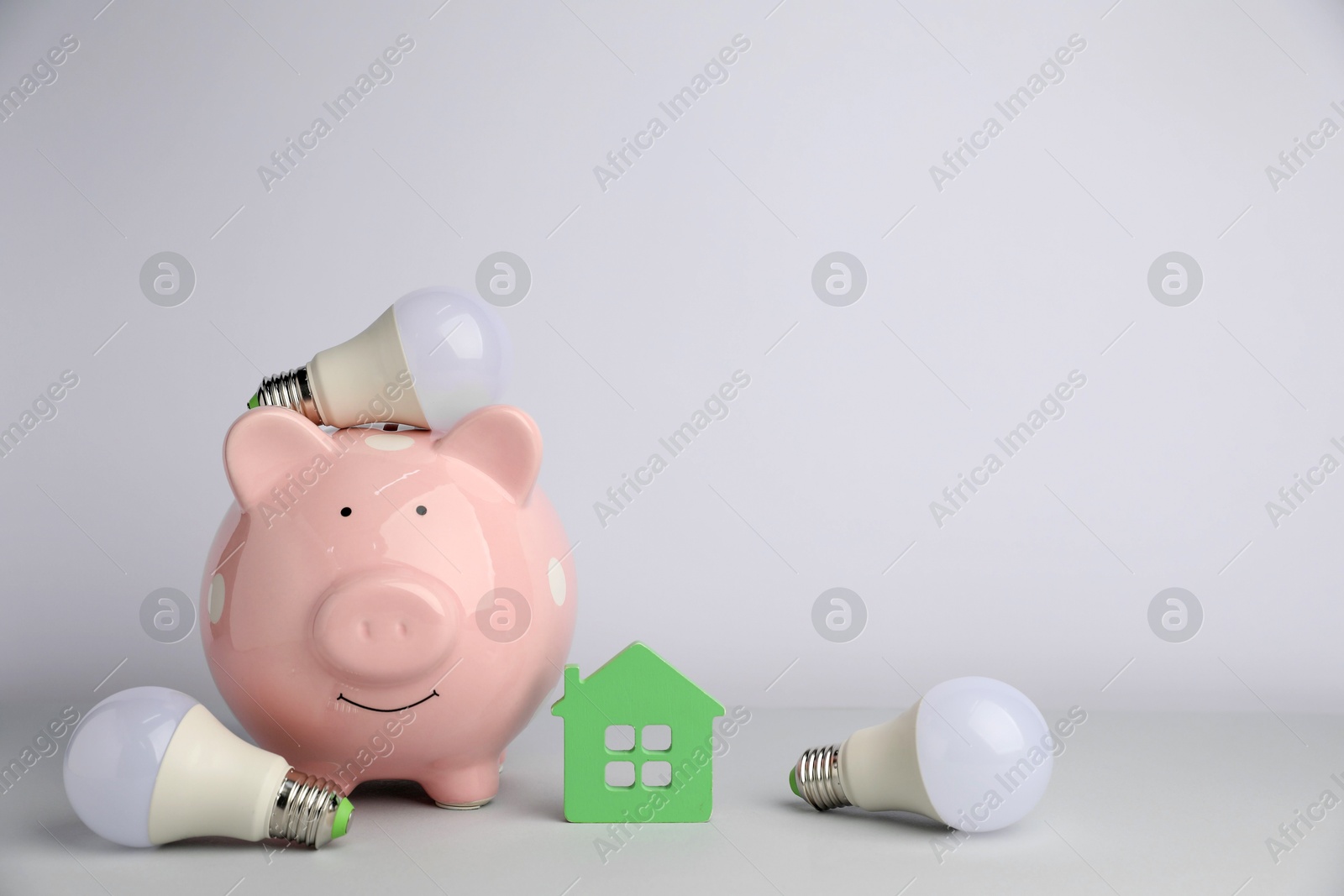 Photo of Piggy bank, house model and light bulbs on grey background. Energy saving concept