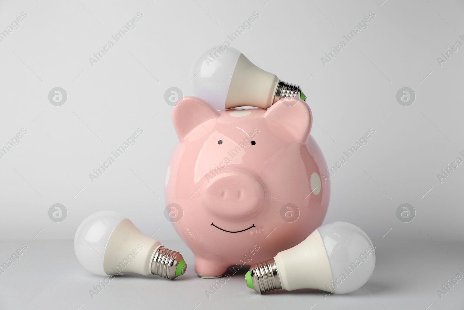 Photo of Piggy bank and light bulbs on grey background. Energy saving concept