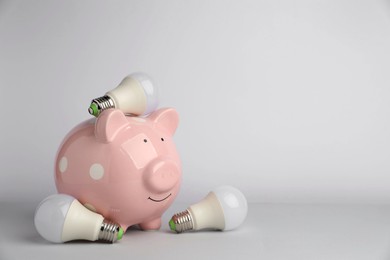 Photo of Piggy bank and light bulbs on grey background, space for text. Energy saving concept