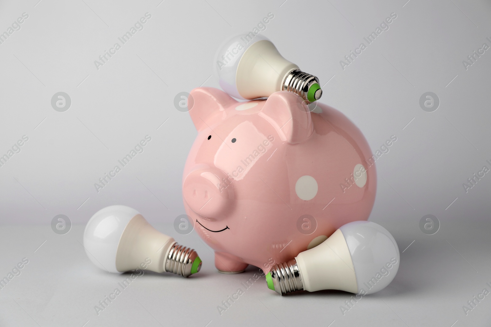 Photo of Piggy bank and light bulbs on grey background. Energy saving concept