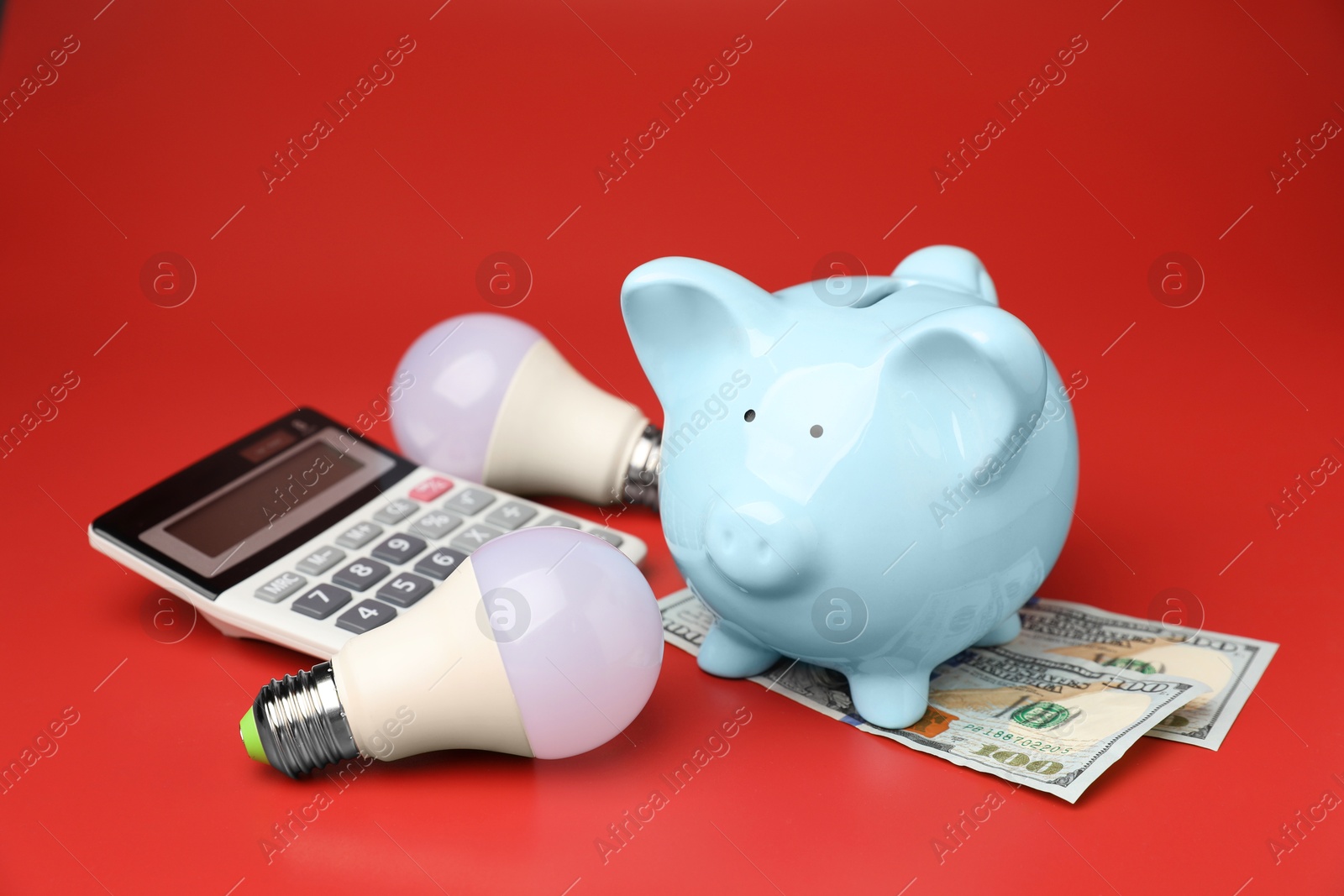 Photo of Piggy bank, dollar banknotes, calculator and light bulbs on red background. Energy saving concept