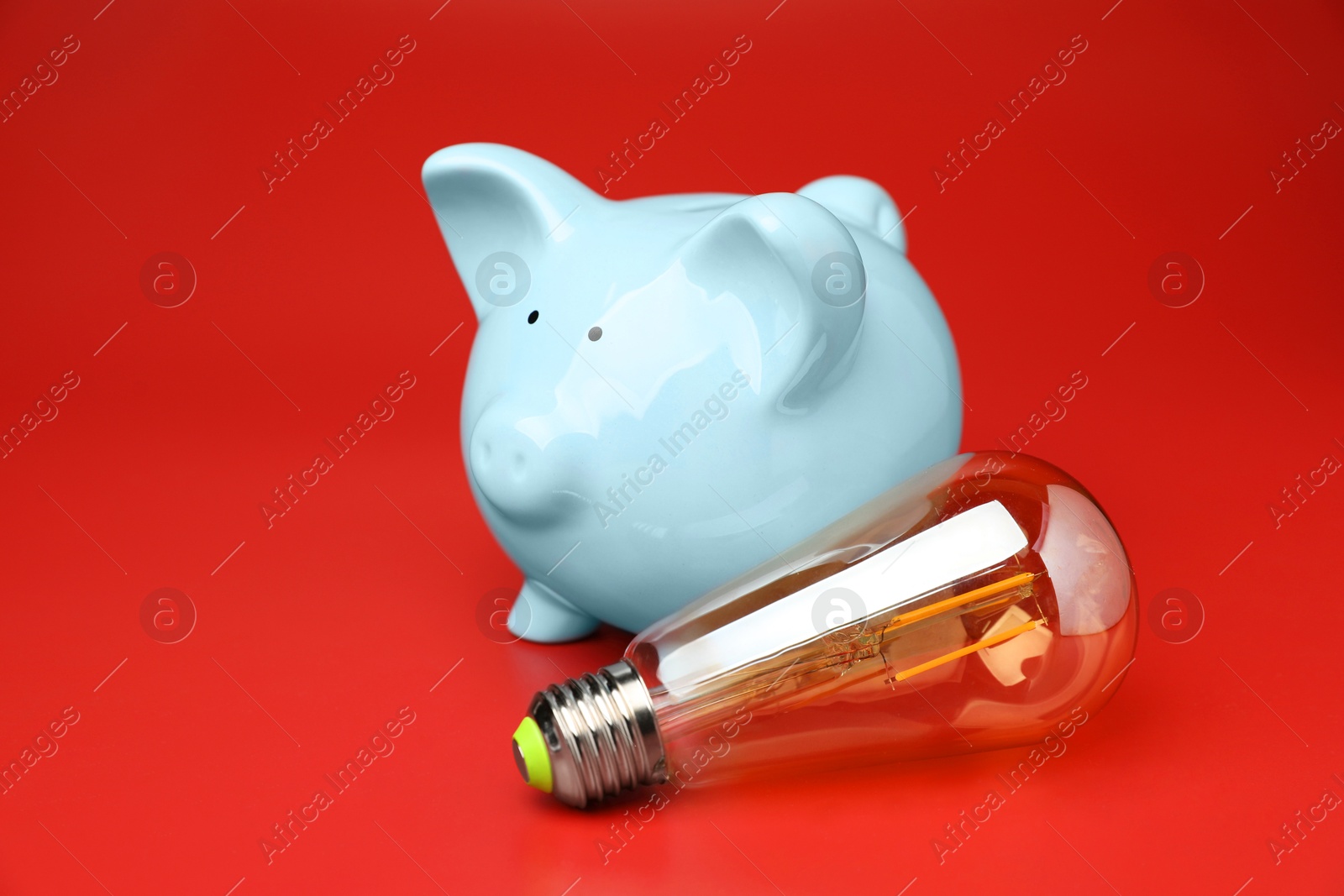 Photo of Piggy bank and light bulb on red background, space for text. Energy saving concept