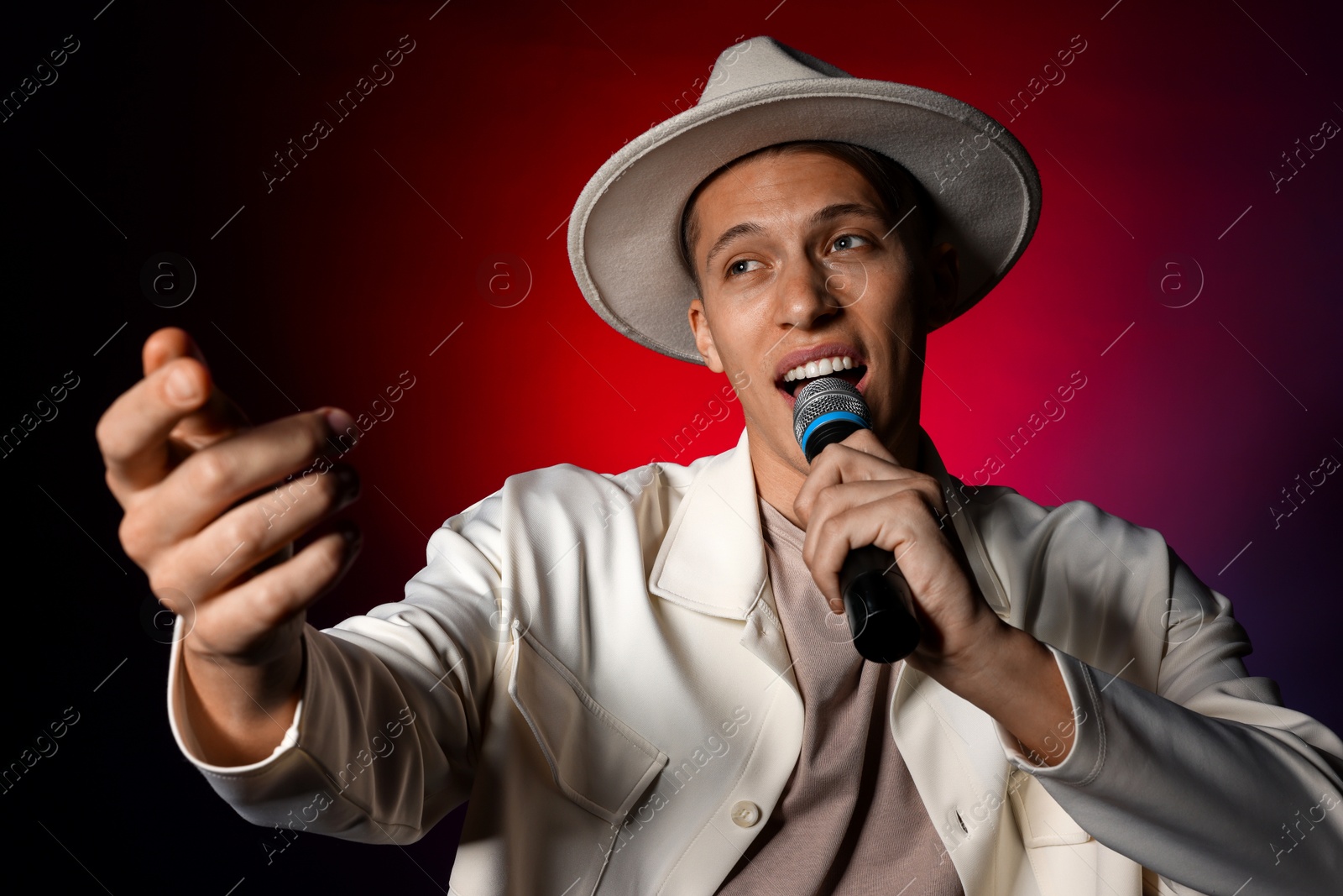 Photo of Talented young man singing on dark background with red light