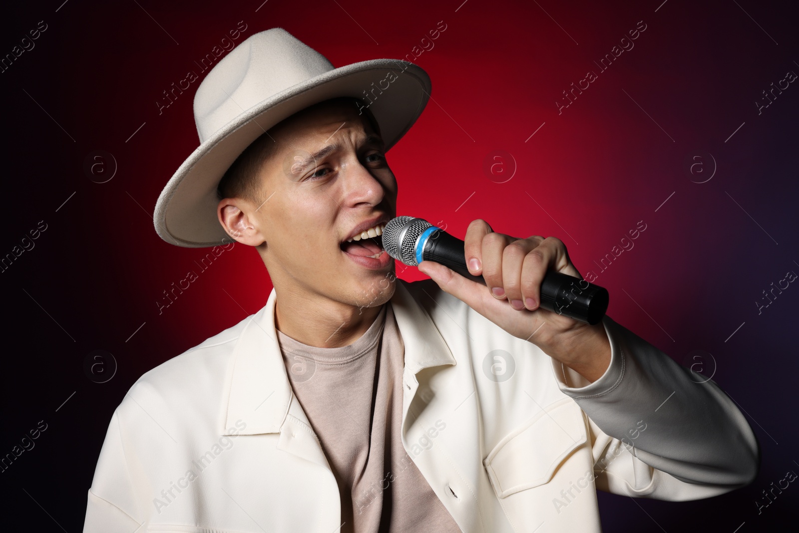 Photo of Talented young man singing on dark background with red light