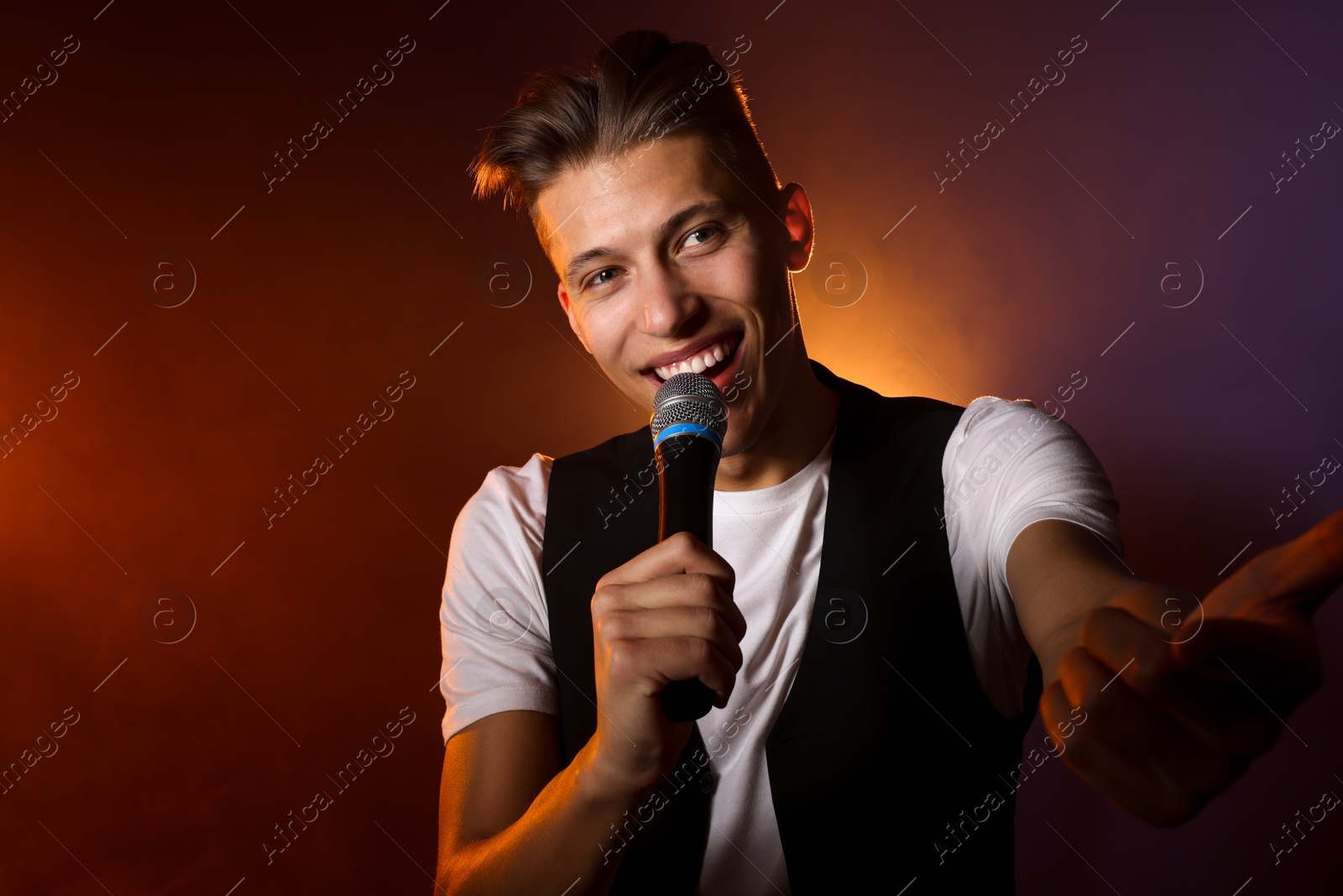 Photo of Talented young man singing on dark background with color light