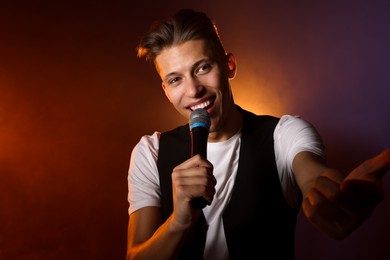 Photo of Talented young man singing on dark background with color light