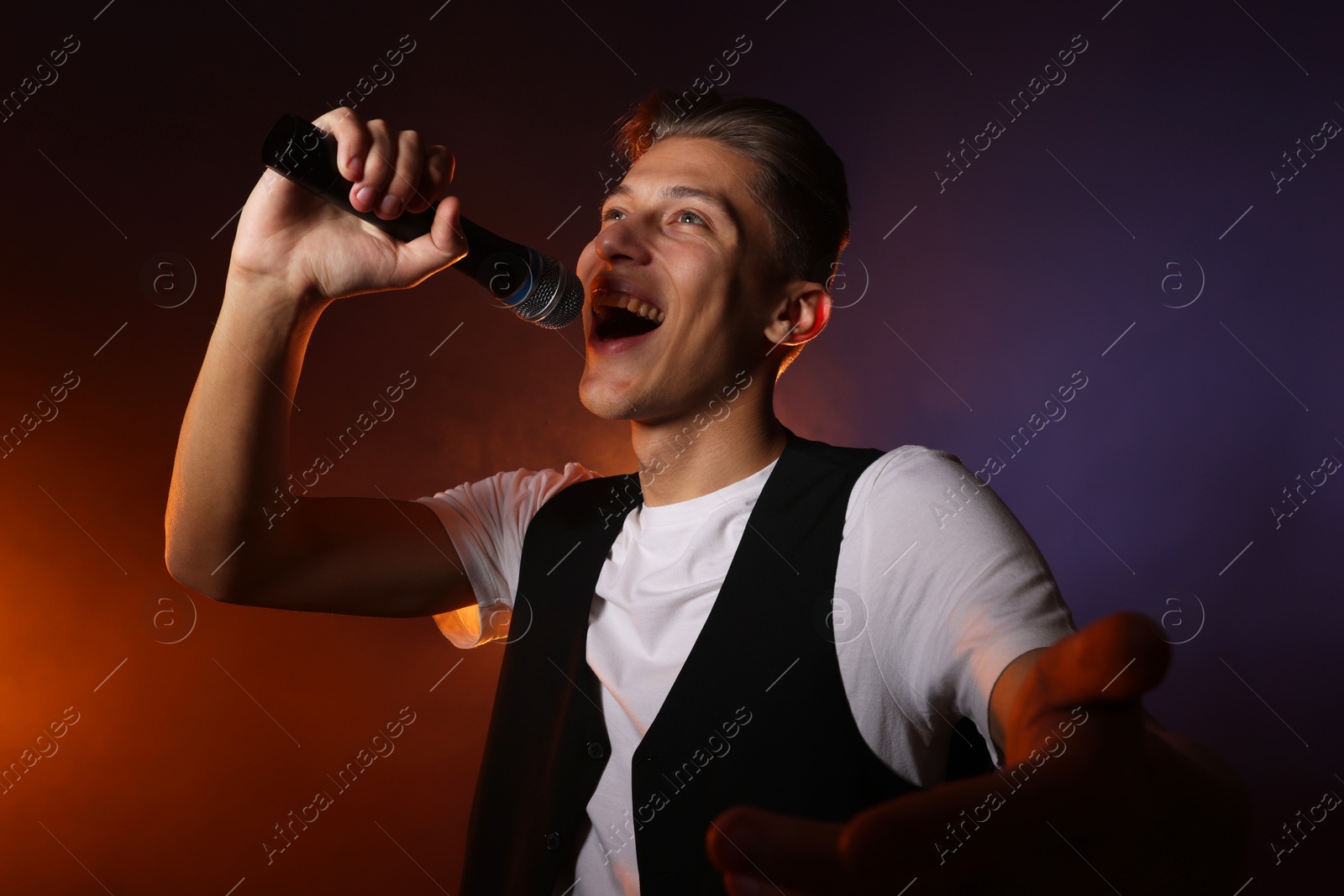 Photo of Talented young man singing on dark background with color light