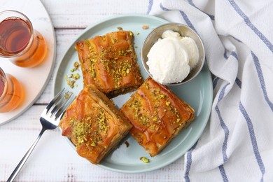 Photo of Delicious baklava with crushed nuts and ice cream served on light wooden table, flat lay