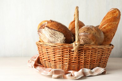 Photo of Different freshly baked bread loafs in wicker basket on white wooden table, closeup