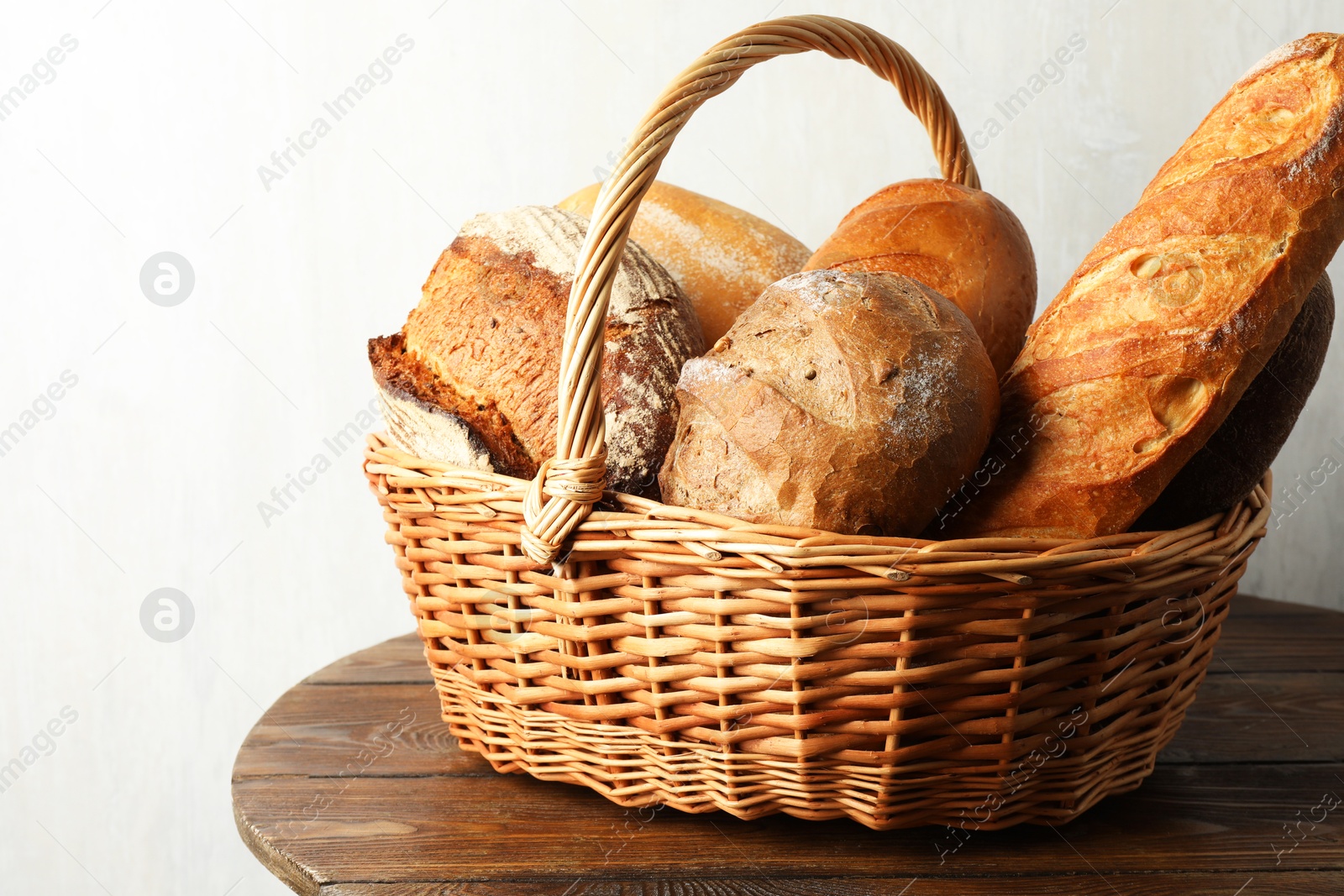 Photo of Different freshly baked bread loafs in wicker basket on wooden table, closeup