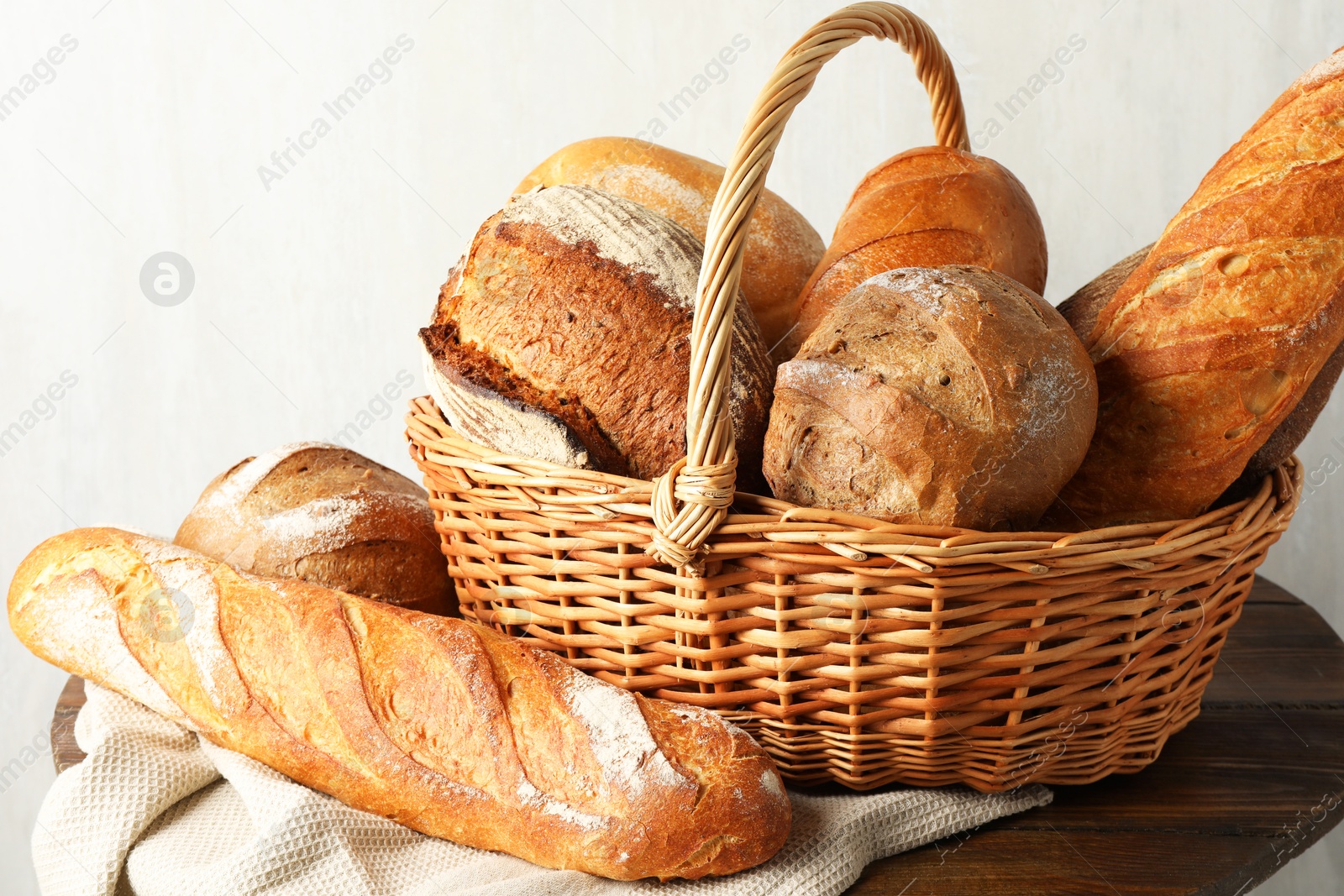 Photo of Different freshly baked bread loafs and wicker basket on wooden table, closeup