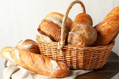 Photo of Different freshly baked bread loafs and wicker basket on wooden table, closeup