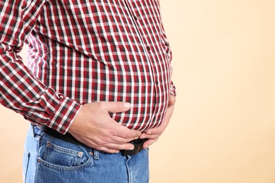 Photo of Overweight man in tight shirt on beige background, closeup. Space for text