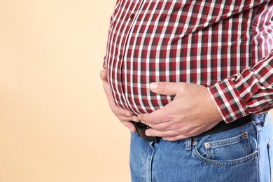 Photo of Overweight man in tight shirt on beige background, closeup. Space for text