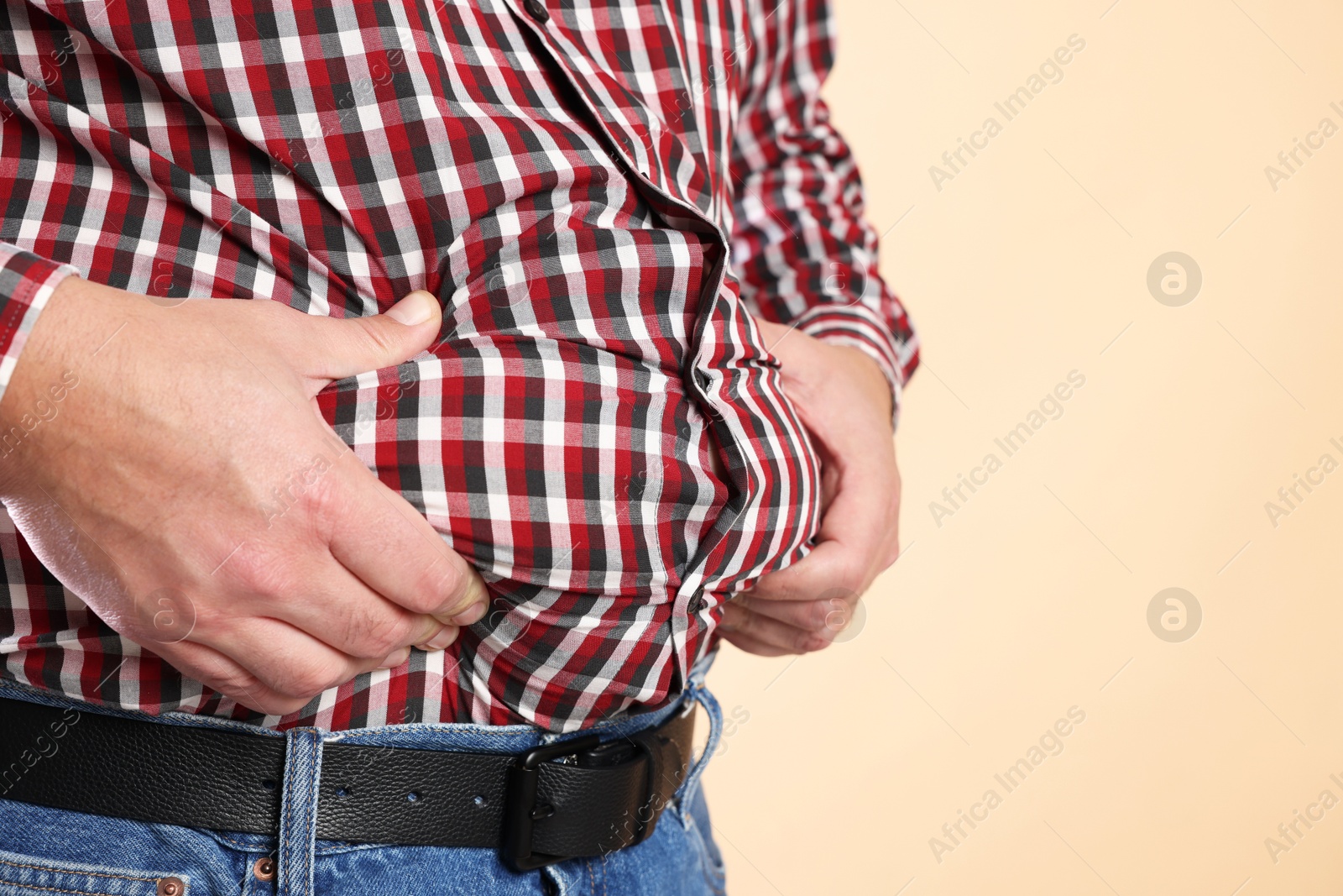 Photo of Overweight man in tight shirt on beige background, closeup. Space for text