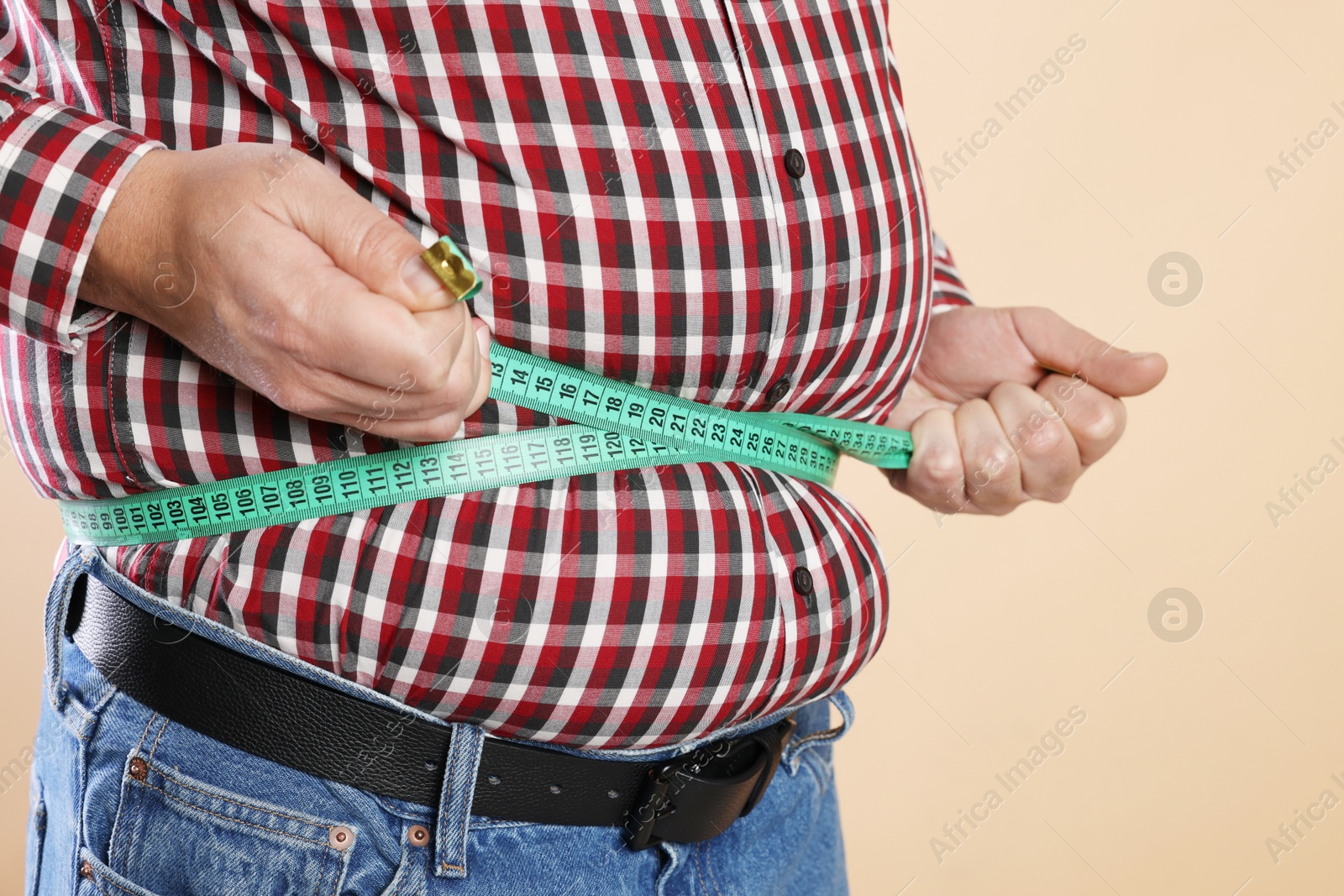 Photo of Overweight man measuring his belly with tape on beige background, closeup