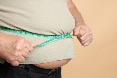 Photo of Overweight man measuring his belly with tape on beige background, closeup