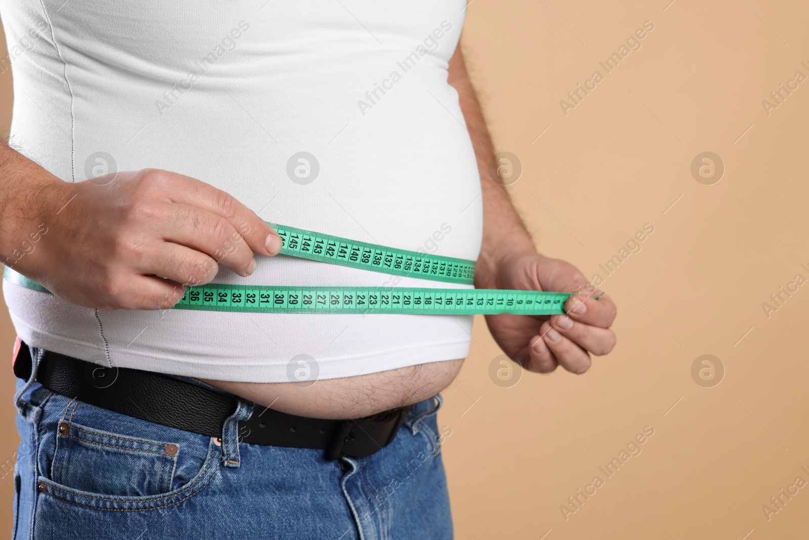 Photo of Overweight man measuring his belly with tape on beige background, closeup. Space for text