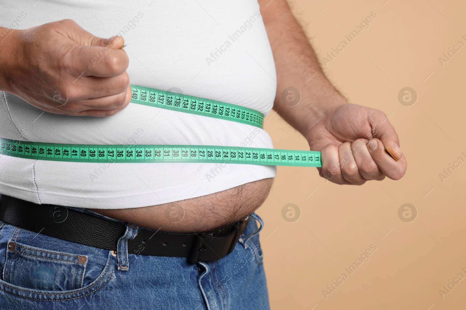 Photo of Overweight man measuring his belly with tape on beige background, closeup