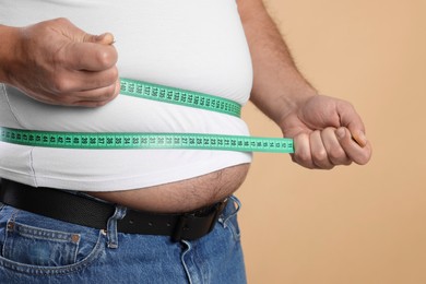 Photo of Overweight man measuring his belly with tape on beige background, closeup