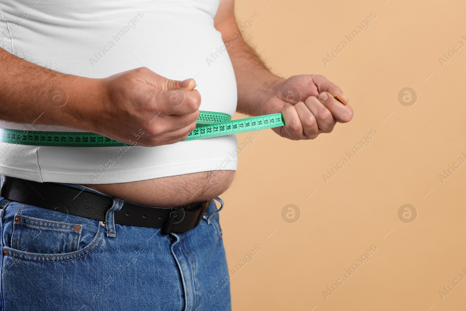 Photo of Overweight man measuring his belly with tape on beige background, closeup. Space for text